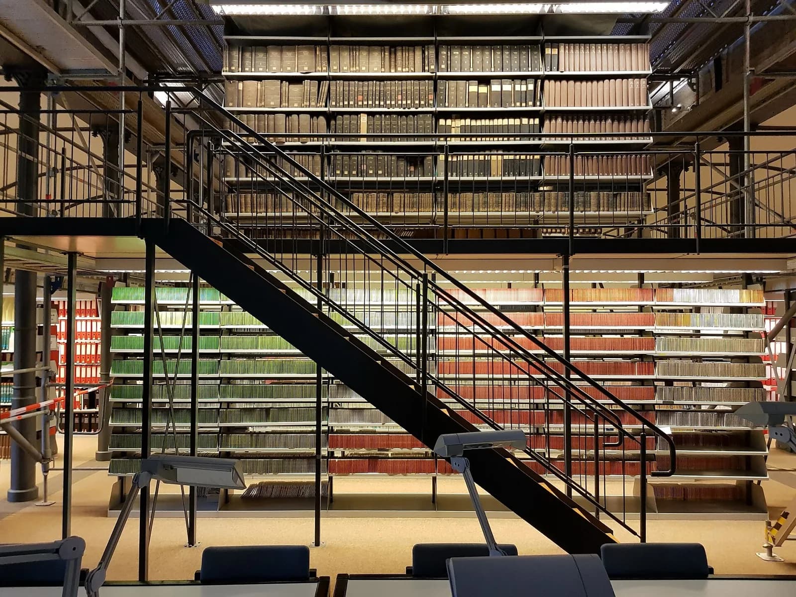 Sala de una biblioteca con estanterías de volúmenes y puestos de lectura en primer plano